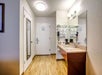 Hotel bathroom with a wooden floor, large mirror, sink, and toiletries. Wall-mounted hairdryer and towels are neatly arranged. Door to the room is visible.