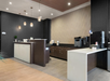 Modern hotel front desk area with two check-in counters, pendant lights, a coffee machine, office equipment, and minimalist decor.