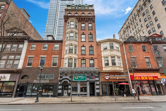 A row of mixed-use buildings with shops at street level, including a restaurant, brow bar, and offices; taller modern buildings are visible in the background.