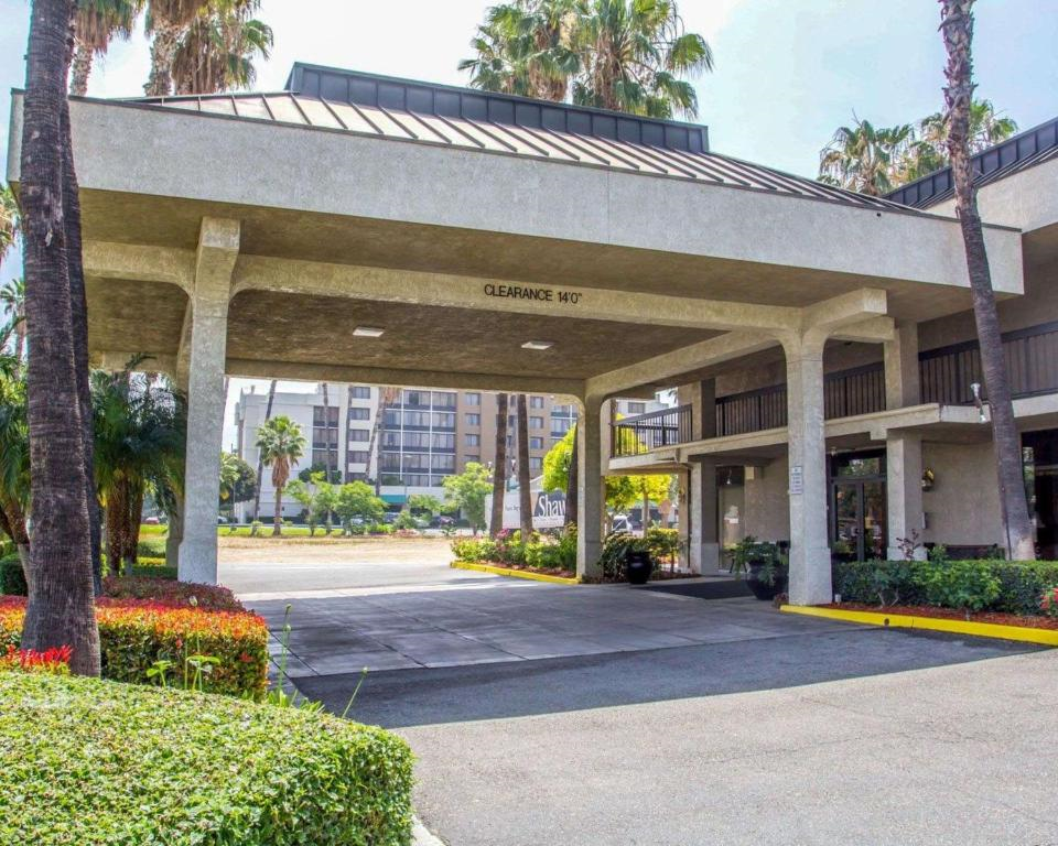 Hotel entrance with a covered driveway and palm trees, leading to a building with multiple floors. Nearby buildings are visible in the background.