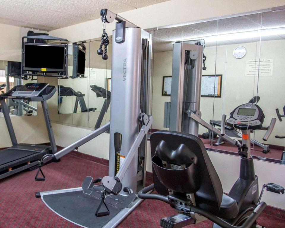A gym room with exercise equipment including a treadmill, a weight machine, and a stationary bike, reflected in a large mirror.