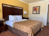A king bed, two side tables with lamps, and small red and yellow painting on the wall in a guest room.