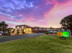 Quality Inn building at sunset with a sign for RV and boat parking. Sky shows vibrant hues of pink and purple. Grass and trees in the foreground.