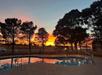 Sunset over a swimming pool with reflections of pine trees and vivid orange and pink hues in the sky.