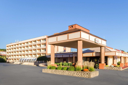 Large hotel building with multiple floors and a rectangular entrance canopy. There are plants in front of the entrance and a clear blue sky.