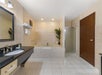 Spacious bathroom with a large bathtub, separate glass shower, single sink vanity, tiled floors, and beige walls. Towels and toiletries are neatly arranged.