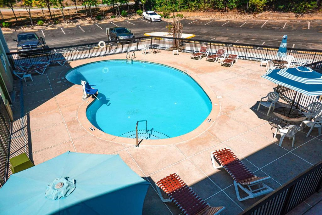 Outdoor swimming pool surrounded by a fence, with several lounge chairs and umbrellas. A wheelchair lift is on the left side. Parked cars visible in the background.