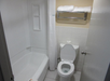 Small bathroom with a white bathtub-shower combo, toilet, and a wall-mounted towel rack with white towels. Beige walls and white tiles.