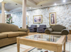 A hotel lobby with brown sofas, a glass coffee table, and three framed paintings on a stone wall backdrop.
