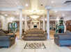 Spacious hotel lobby with beige sofas, decorative pillars, plants, and a geometric tile design on the floor.