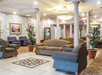 A hotel lobby with patterned tile flooring, armchairs, sofas, and potted plants. There is a large light fixture on the ceiling and a stone accent wall with framed artwork.