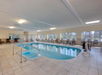 Indoor swimming pool with tiled flooring, surrounded by lounge chairs and large windows providing natural light.