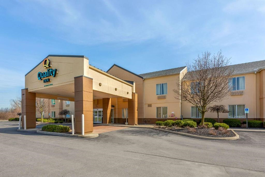Exterior view of a Quality Inn hotel with a beige facade, covered entrance, and landscaped surroundings.