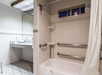 Accessible bathroom with bathtub, grab bars, a shower curtain, tiled walls, and a sink with a mirror in the background.