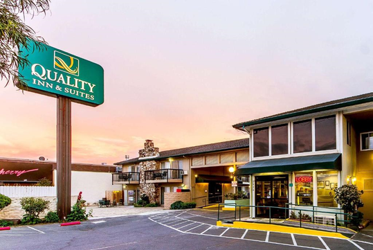 Exterior view of Quality Inn & Suites with a large sign, sunset sky, and entrance to the lobby.
