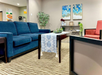 A cozy waiting area with blue and red seating, a patterned rug, decorative plants, and artwork on the wall.