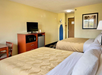 Hotel room with two double beds, flat-screen TV, microwave, mini fridge, a small dining table with chairs, an ironing board, and a hallway leading to the door.