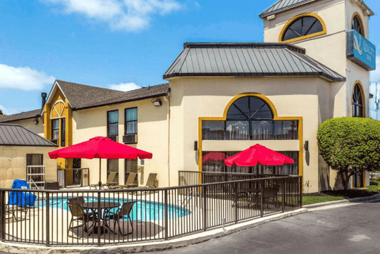 The light tan exterior of the Quality Inn at the Park with yellow trim around the windows and a small outdoor pool on a sunny day.