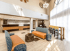 A hotel lobby with a sitting area with blue and orange couches and a tall table next to floor to ceiling windows with the front desk in the background.