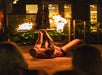 A fire performer lies on their back, balancing a flaming baton with their feet during an outdoor nighttime show.