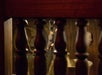 A bat hangs upside down between ornate wooden balusters in a dimly lit space.