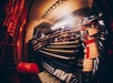 Close-up of a large, intricate pipe organ keyboard with multiple rows of keys, stops, and pedals. The surrounding area is dimly lit with red lighting.
