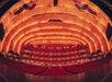 A wide-angle view of an empty theater with illuminated golden arches and rows of red seats.