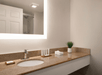 A bathroom with a granite countertop, round sink, modern faucet, potted plant, folded towels, toiletries, and a lit mirror. The shower and door are visible in the background.