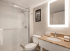 Modern bathroom with a walk-in shower, toilet, and sink. A mirror with backlighting hangs above the countertop. A framed photo decorates the wall.