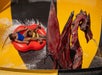 Two people on a red inflatable raft slide past a large dragon statue in a yellow and black water park ride.
