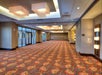 Spacious empty banquet hall with patterned carpet, wall lights, large windows, and modern ceiling fixtures.