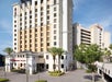 A multi-story Ramada Plaza hotel with palm trees and a parking garage in the background under a clear blue sky.