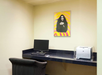 A small office space with a desk featuring a computer and a printer. A framed poster of a woman with a colorful background is on the wall above.