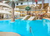 Indoor water park with blue pool, large waterslide, and a pirate ship-themed play structure. Palm trees and seating area visible in the background.