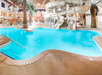 Indoor water park with a swimming pool, slides, palm trees, and a seating area.