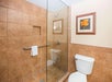 Bathroom with a glass-enclosed shower, tiled walls, a framed floral picture, and a white toilet. There's a towel on the shower's grab bar.