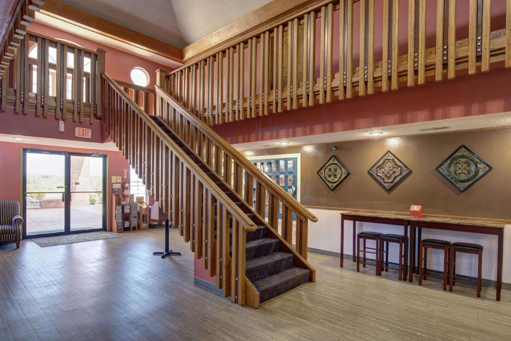 Hotel lobby with wooden staircase, red walls, decorative wall art, a table with chairs, and a glass entrance door.