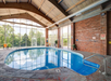 Indoor swimming pool with a vaulted wooden ceiling, brick walls, and large windows displaying a view of trees outside. A "No Diving" sign is visible on the wall.