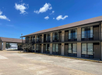 Two-story motel building with exterior corridors, set against a clear blue sky. Each unit has a window and a door, with outdoor stairs leading to the second floor. Parking lot in foreground.