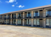 Two-story motel building with exterior entry doors and windows. Upper level accessed by a staircase. Clear blue sky overhead.
