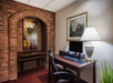 A small office space with a desk and chair, computer, lamp, and artwork on a brick-accented wall.