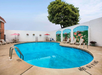 Outdoor swimming pool surrounded by lounge chairs and umbrellas, with a painted mural on the wall and a large tree in the background.