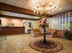 Hotel lobby with a floral arrangement on a round table, chandelier, two sofas, a front desk, and framed artworks on the wall.