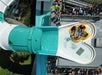 A group of people in a yellow raft exits a large enclosed water slide into a shallow pool while others wait in line above.