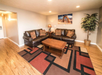 Living room with two brown leather sofas, a wooden coffee table, and a patterned rug. There is a potted plant and landscape art on the wall. Wood flooring and recessed lighting complete the space.