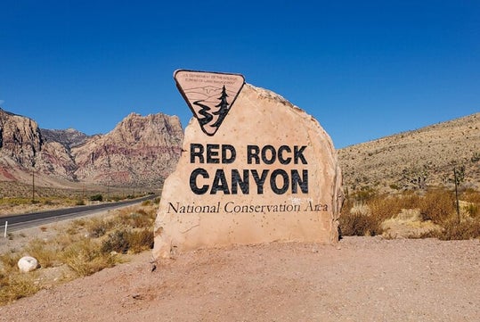 A large stone sign at the entrance of Red Rock Canyon National Conservation Area, with mountains and desert landscape in the background.