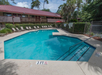 Outdoor swimming pool with lounge chairs and a metal railing. Surrounded by a fence and greenery, with a two-story building in the background. Depth markers indicate 3 feet.
