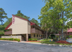 Two-story hotel building with beige walls and a red roof, surrounded by trees and a parking area.