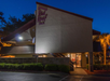 Exterior view of a Red Roof Inn building at night, with illuminated signage and surrounding greenery.