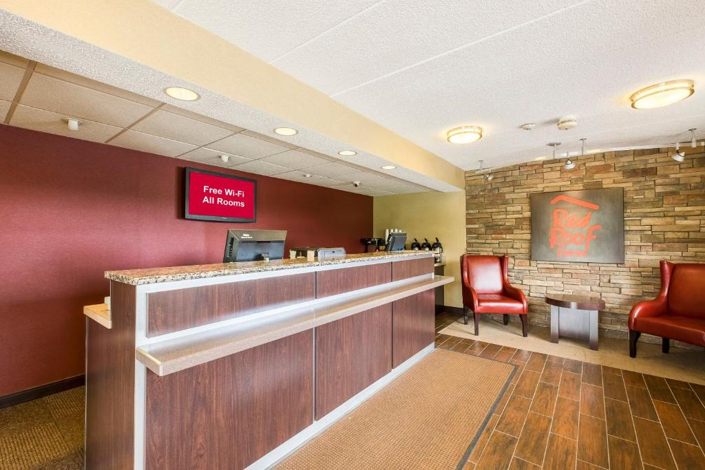 Hotel lobby with a front desk and a digital sign displaying "Free Wi-Fi All Rooms." Two red chairs and a sign on a brick wall are in the background.